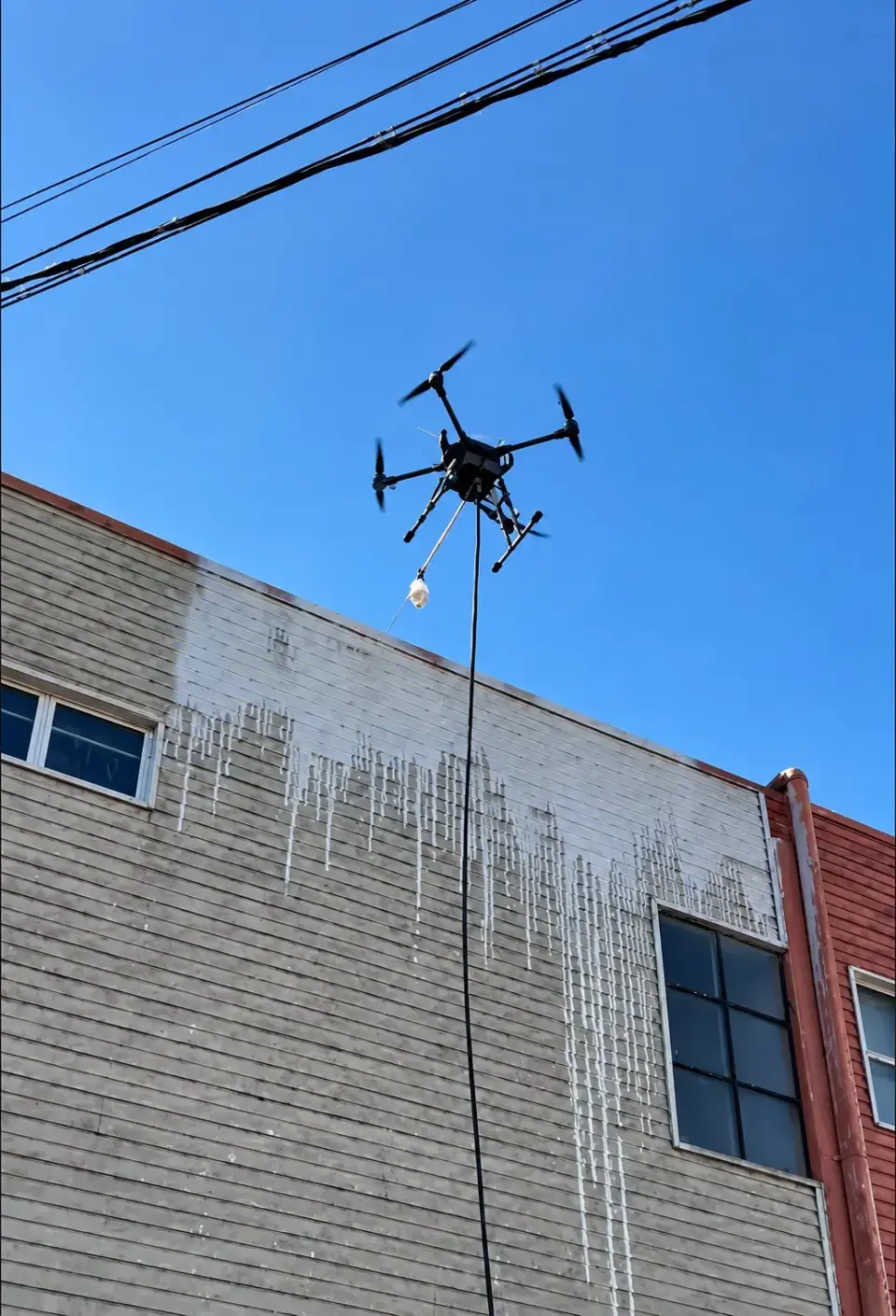 Drone aplicando solução de limpeza na fachada de um galpão industrial em Hortolândia