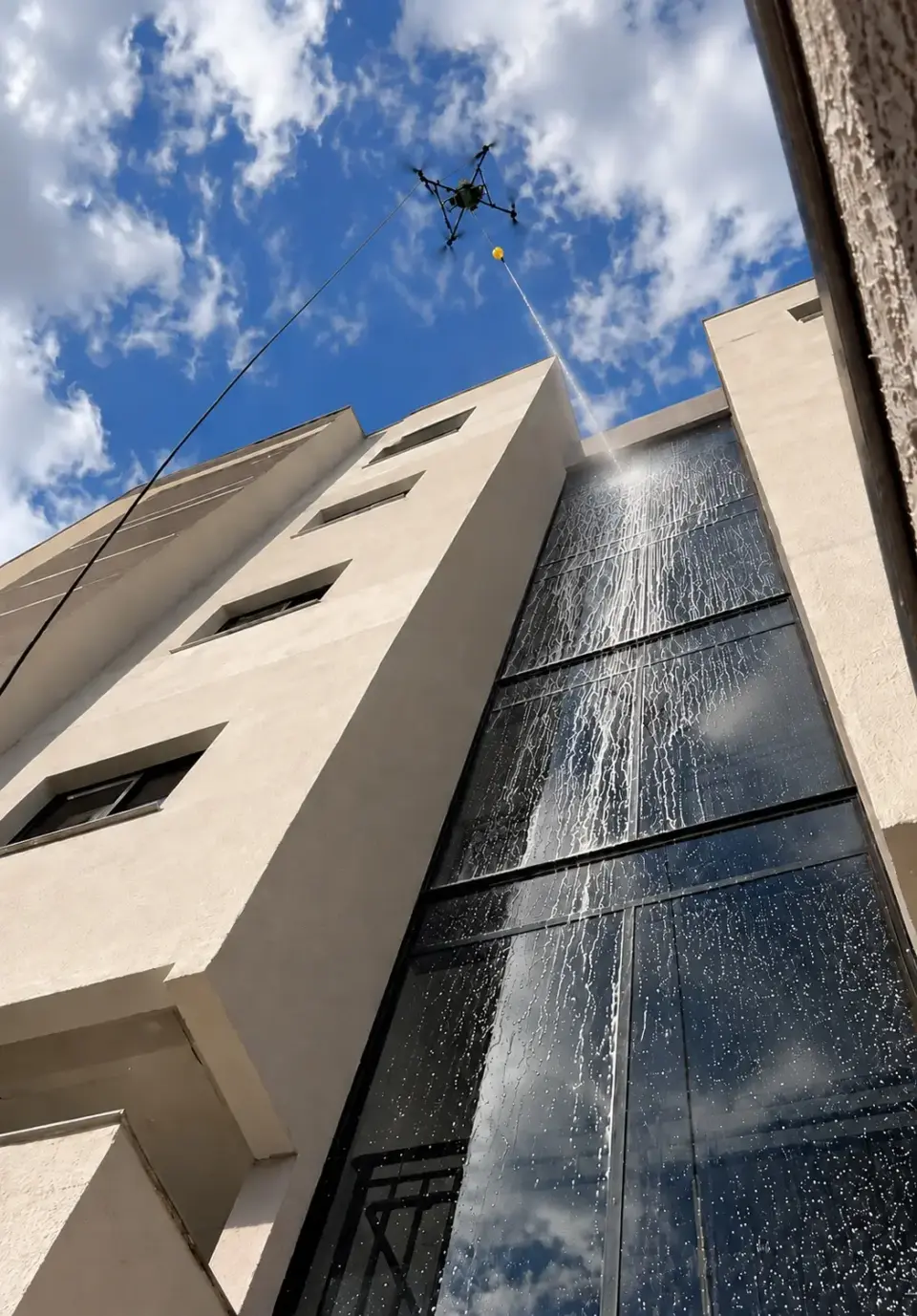 Fachada de vidro do prédio residencial molhada durante a limpeza com drone