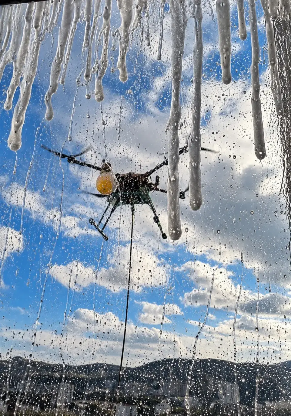 Gotas de água escorrendo no vidro com o drone de limpeza ao fundo