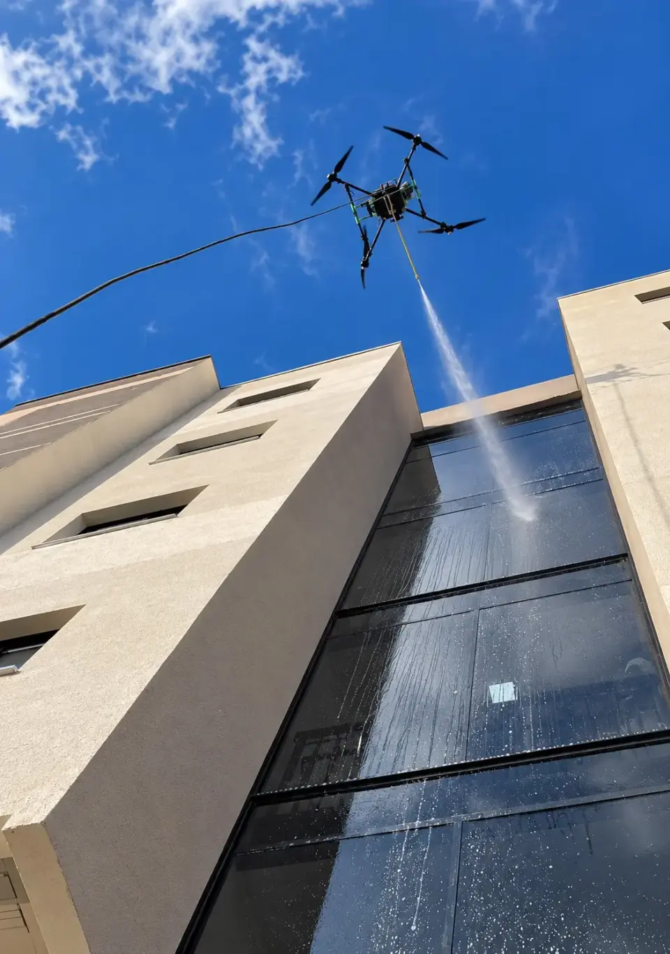 Drone com mangueira aplicando água na fachada de vidro do prédio